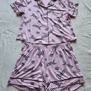 Juicy Couture rosa pyjamas set XL - Säljer ett par supermjuka rosa pyjamasshorts från Juicy Couture med svart logotyp- och kronmönster över hela tyget. Shortsen har elastisk midja och svarta passpoaldetaljer längs bensluten. Perfekta för mysiga hemmakvällar.