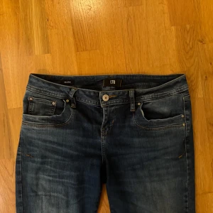 Mörkblå jeans från LTB Valerie - Snygga mörkblå lågmidjade jeans från LTB, modell Valerie. Klassisk femficksdesign med orangea sömmar och raka ben/bootcut. Jeansen har en lätt tvättad look. Är i storlek 30x30 (passar M-L).