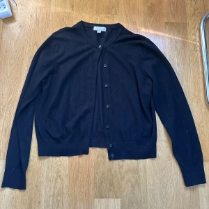 Svart kofta från H&M i bomull - Svart klassisk kofta från H&M i storlek L. Den har rund hals, långa ärmar och knappar framtill. Materialet är mjuk bomull som känns skönt mot huden. Perfekt att slänga över en t-shirt eller linne.