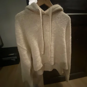 Stickad Zara hoodie - Mysig beige stickad hoodie från Zara med huva och snörning. Tröjan har lång ärm, ribbade muddar och en lite loose passform. Perfekt för kyliga dagar och enkel att matcha med jeans eller leggings.