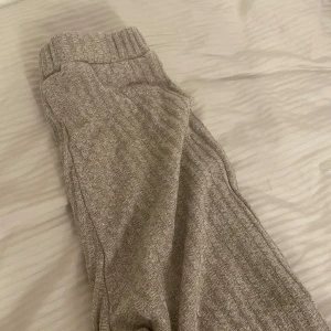 Beige ribbade stickade byxor - Mysiga stickade byxor i beige med ribbad struktur och bred resår i midjan. Perfekta för chill dagar hemma eller när du vill vara extra bekväm. Byxorna har en rak passform och är gjorda i ett mjukt material som känns skönt mot huden.