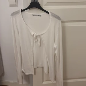 Vit kofta med knyt från 157 - Superfin vit kofta från 157 med knyt framtill och långärmad modell. Tunn och mjuk i materialet, perfekt för lager-på-lager. Enkel och stilren design som passar till allt. Jätte söt!