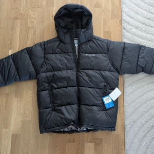 Helt ny Columbia Pike Lake II med tags  - Pris i butik: 2199:- Mitt pris: 999:-. En jacka tillverkad för vardaglig komfort i kylan hela dagen, var du än är. Ett avancerat termiskt reflekterande foder fångar värme medan isolering i 100 % återvunnen polyester ger värme. Funktioner inkluderar PFC-fri vattenavvisande förmåga, säkerhetsdragkedja och handfickor samt justerbar huva, fåll och manschetter. Omni-Heat" termiskt reflekterande isolering tillverkad av 100 % återvunnen polyester Justerbar huva med dragsko Hakskydd