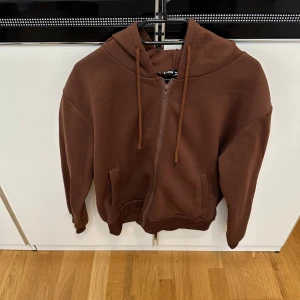 Brun kofta/hoodie med dragkedja från SHEIN - Brun hoodie/kofta från SHEIN med hel dragkedja framtill, huva och snörning. Koftan har två fickor och ribbade muddar vid ärmslut och nederkant. 