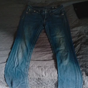 Miss Me blå jeans med detaljer - Snygga blå jeans från Miss Me med broderade bakfickor med strassdestaljer. Jeansen har klassisk femficksdesign och är tillverkade i bomull med lite stretch för skön passform. Perfekta för dig som gillar jeans med extra detaljer.