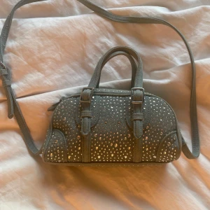 Efterfrågad jeansväska från zara - Cool väska i jeansmaterial med glittrande nitar över hela väskan. Den har både handtag och lång axelrem, samt snygga spänndetaljer framtill. Väskan stängs med dragkedja och har en rymlig insida för dina viktigaste grejer.