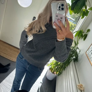 Mörkgrå stickad offshoulder-tröja - Mysig mörkgrå stickad tröja med offshoulder-design och lång ärm. Tröjan har en avslappnad passform och ribbade muddar vid ärmslut och nederkant. Perfekt för lager-på-lager och chill dagar.