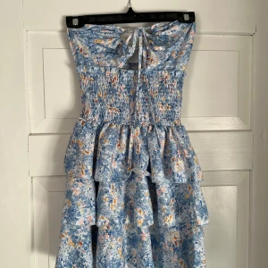 Blommig blå volangklänning med knyt - Supersöt kort klänning i ljusblått med blommigt mönster och volanger. Perfekt för varma dagar och ger en romantisk vibe. Går att knyta på olika sätt. Pris kan diskuteras 