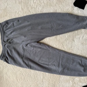Grå mjukisbyxor från H&M Relaxed Fit - Grå mjukisbyxor från H&M i relaxed fit med resår och snörning i midjan. Byxorna har en bakficka och är tillverkade i mjukt bomullsmaterial. Perfekta för chill dagar eller när du vill vara extra bekväm.