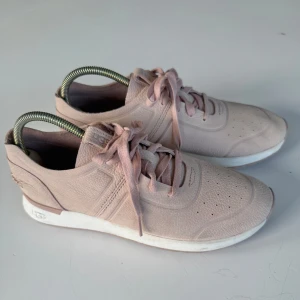 Ljusrosa sneakers från UGG i skinn - Säljer ett par ljusrosa sneakers från UGG i mjukt skinn med snörning och vit sula. Skorna har en stilren design med diskret UGG-logga på sidan och plösen. Perfekta för dig som gillar en clean och modern look.