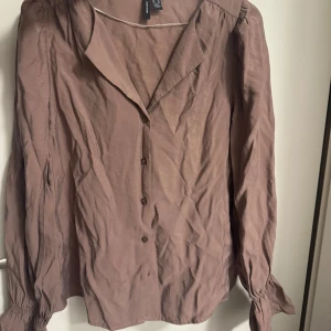Brun skjorta  - Snygg brun skjorta från H&M med långa ärmar och knyt vid ärmsluten. Skjortan har en v-ringad krage och knappar framtill. Tillverkad i mjuk bomull, perfekt för dig som gillar en chill och stilren look.