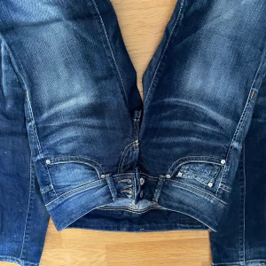 Mörkblå jeans från Pepe Jeans - Snygga mörkblå jeans från Pepe Jeans med klassisk femficksdesign, slitningar och kontrastsömmar. Jeansen har raka ben och knappgylf, samt Pepe Jeans-logga på bakfickan. Perfekta för en avslappnad och cool stil.