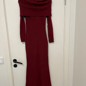 Vinröd långärmad långklänning - Snygg vinröd långklänning med långa ärmar och bred, draperad krage som ger en cool offshoulder-look. Klänningen är figurnära och har en elegant, enkel design som passar perfekt när du vill sticka ut. Materialet är mjukt och stretchigt för en bekväm känsla.