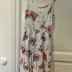 Vit blommig sommarklänning  - Superfin vit klänning från hm med röda och rosa blommor, smala axelband och smockad rygg. Lätt och luftig modell som är perfekt för varma dagar. Klänningen har en avslappnad passform och är tillverkad i mjuk bomull. Stl 32