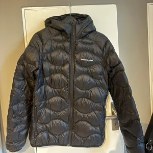 Svart dunjacka Peak Performance M - Svart dunjacka från Peak Performance”HELIUM DOWN HOOD JACKET DAM” i storlek M. Jackan har huva, dragkedja framtill, fickor på sidorna och en design med vågigt mönster. Finns ett litet hål på armen( se bilden). Priset går att diskuteras! 😊