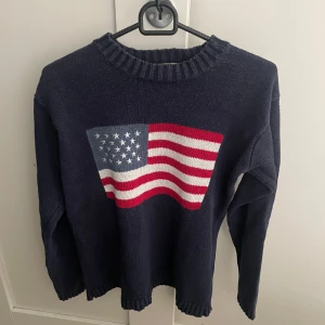 Mörkblå stickad tröja med USA-flagga - Mörkblå stickad tröja med en USA flagga på i storlek M, modellen är ca 180 lång. Hör av dig vid funderingar!