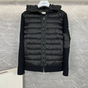 Svart Moncler cardigan alla storlekar finns tillgängliga  - Svart pufferjacka från Moncler med stickade ärmar och quiltad front. Jackan har en avtagbar huva med snörning, dragkedja framtill och ficka med knapp på ena ärmen. Perfekt för kyliga dagar och riktigt snygg streetstil.