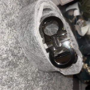 Svart skärp från Salvatore Ferragamo - Snyggt svart bälte från Salvatore Ferragamo i äkta skinn med ikoniskt metallspänne i silverfärg. Bältet har en stilren och klassisk design med präglad storleksmärkning på insidan. Perfekt accessoar för att lyfta din outfit.