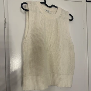 Vit stickad väst från ONLY - Vit, ribbstickad väst från ONLY med rund halsringning och breda axelband. Västen har en enkel och clean look, perfekt att styla över en skjorta eller t-shirt. Tjockare ribbad kant nedtill för en snygg finish.