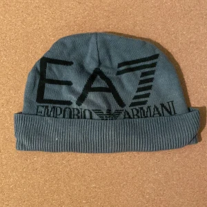Blå EA7 Emporio Armani mössa - Snygg grå  mössa från EA7 Emporio Armani med stor svart logga framtill. Mössan 