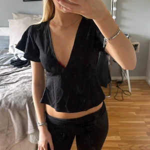 Svart omlottopp med v-ringning - Svart omlottopp med djup v-ringning perfekt till fest🥰från Gina i storlek xs 