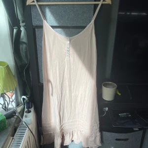 Ljusbeige sommarklänning från Culture - Supersöt ljusbeige klänning från Culture med smala axelband, knappar framtill och volangdetalj längst ner. Klänningen har en avslappnad passform och är tillverkad i ett mjukt, tunt material som känns svalt mot huden. Perfekt för varma dagar!