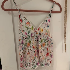 Blommig broderad linnetopp med spets - Superfin linnetopp med blommigt mönster i pastellfärger och broderade hålbroderier. Toppen har smala justerbara axelband, v-ringning och en croppad passform. Spetsdetaljer längs kanterna och en luftig känsla gör den perfekt för varma dagar.😊🤩