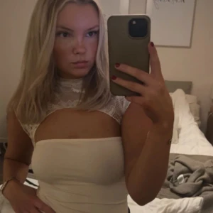 Vit spetsklänning med cut out-detalj - Supersnygg vit klänning med hög hals i spets och trendig cut out-detalj över bröstet. Tight passform som framhäver figuren och ärmlös design. Perfekt för dig som vill sticka ut med en modern och feminin look. Från VENDERBYS! 