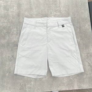 Vita shorts från Peak Performance - Snygga vita shorts från Peak Performance med klassisk passform och bälteshällor. De har fickor fram och en bakficka med dragkedja. Perfekta för sommardagar och sportiga aktiviteter. Materialet känns mjukt och lätt, vilket gör dem riktigt bekväma.