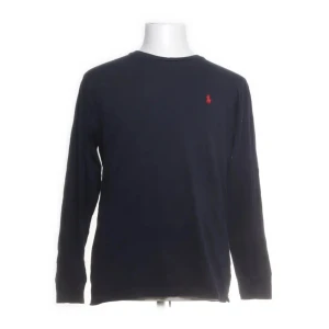 Mörkblå långärmad tröja Polo Ralph Lauren - Klassisk mörkblå långärmad tröja från Polo Ralph Lauren i 100% bomull. Tröjan har rund halsringning och den ikoniska röda loggan broderad på bröstet. Perfekt för en stilren och avslappnad look.