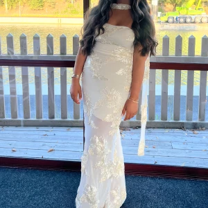 Vit långklänning med blommig spets - Beige långklänning med blommig spets och axelbandslös design. Har endast används några timmar. Förlängt under kjol hos skräddaren plus kortat ner kläningen. 