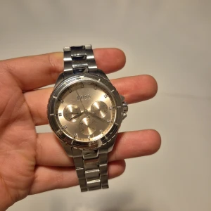 Stilren silverklocka från BOSS - PROTECTIVE RUBBER LAYER IS STILL ON, NO SCRATCHES. New prive 2600 SEK. Säljer en snygg och klassisk klocka från BOSS med rund urtavla i champagnefärg och tre mindre subdials. Klockan har en robust länkad armlänk i silverfärgat metall och tydliga indexmarkeringar med små stenar. Perfekt accessoar för dig som gillar stilren design.