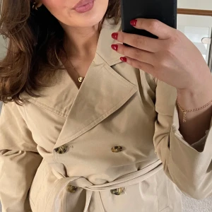 Beige trenchcoat med bälte - Snygg beige trenchcoat med dubbelknäppning och knytskärp i midjan. Passar en XS/S. Fint skick då jag ej använt den så mkt. Köpte i våras för 600. Säljer för 399. Kan gå ner i pris vid snabb affär! Ge pris förslag🥰🥰