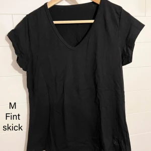 Svart v-ringad t-shirt i bomull M - Enkel svart t-shirt med v-ringning och korta ärmar. Tillverkad i mjuk bomull och har en klassisk passform. Perfekt basplagg för garderoben och lätt att matcha med allt.