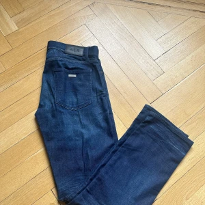 Mörkblå jeans Armani Exchange J16 - Snygga mörkblå jeans från Armani Exchange, modell J16 Straight. Klassisk femficksdesign med raka ben och diskret logga på bakfickan. Jeansen är tillverkade i ett slitstarkt denimtyg och har en stilren look som passar till det mesta.