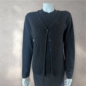 Svart kofta och topp med pärlor - Svart kofta med matchande ärmlös topp, båda dekorerade med små svarta pärlor framtill. Koftan har rund hals och knappar längs framsidan, medan toppen har ribbad halsringning och sitter snyggt mot kroppen. Perfekt för dig som gillar stilrena detaljer. #kofta #topp