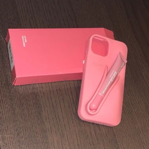 Rhode Lip Case med Peptide Lip Tint - Snygg och praktisk Rhode Lip Case i rosa, designad för att hålla din Peptide Lip Tint nära till hands. Passar iPhone-modeller, tillverkad i slitstark silikon. Produkten är i nyskick, levereras med originalförpackning och medföljer en oöppnad Peptide Lip Tint. Passar till iPhone 13, 14, 15 och iPhone 16e