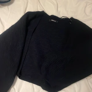 Svart stickad kofta från Gina Tricot - Mysig svart stickad kofta från Gina Tricot i storlek M men passar också som S. Koftan har ett ribbat mönster på både ärmar och framstycke, vilket ger en cool textur. Perfekt att slänga över en t-shirt eller linne när det blir lite kyligt.