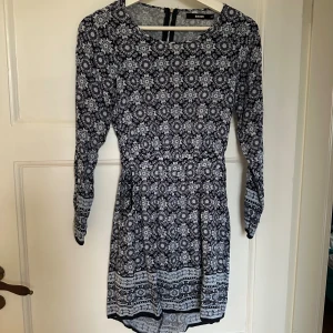 Blommig kortklänning från Bik Bok XS - Supersöt kortklänning från Bik Bok i svart och vitt med blommigt mönster. Klänningen har lång ärm, markerad midja och öppen rygg med dragkedja. Perfekt för dig som gillar unika detaljer och snygg passform.