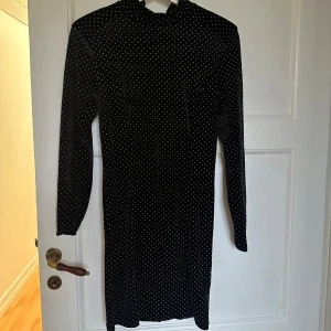 Svart sammetsklänning med prickar BikBok - Supersnygg svart sammetsklänning från BikBok med små vita prickar över hela. Klänningen har lång ärm, figurnära passform och dragkedja i ryggen. Perfekt för dig som gillar en klassisk men ändå trendig look.