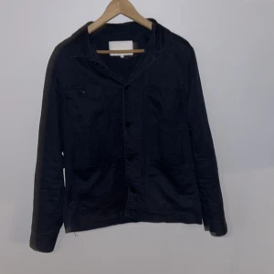 Svart overshirt från Casual Friday - Svart overshirt från Casual Friday i storlek M. Jackan har klassisk krage, knäppning framtill med svarta knappar och flera fickor, inklusive en bröstficka med knapp. Priset står inte skrivet i sten!!!