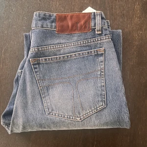 Blå jeans med rak passform - Snygga klassiska blå jeans från Tiger of Sweden med rak passform. Jeansen har en ljus tvätt och bruna detaljer på läderpatchen bak i midjan. Perfekt för dig som gillar tidlös stil och vill ha ett par jeans som funkar till allt.