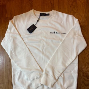 Vit  Polo Ralph Lauren sweatshirt  - Säljer en helt ny vit sweatshirt från Polo Ralph Lauren. Tröjan har långa ärmar, ribbade muddar och är gjord avmjuk bomull. Perfekt för en clean och stilren look. Helt oanvänd och taggarna sitter kvar för endast 600kr