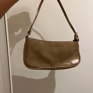 Beige axelväska från Åhléns - Snygg beige axelväska från Åhléns i slät skinnimitation. Väskan har en minimalistisk design med rundade kanter och dragkedja upptill. Perfekt storlek för det viktigaste och enkel att matcha med olika outfits.