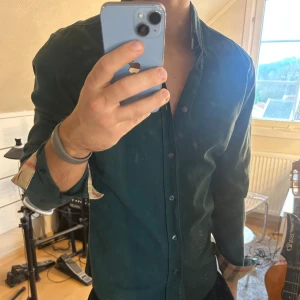 Grön Burberry Brit skjorta i bomull - Snygg grön skjorta från Burberry Brit i mjuk bomull. Klassisk knappstängning och långärmad modell med ikoniskt rutigt tyg på insidan av manschetterna och kragen. Skjortan har en bröstficka och en stilren, normal passform. Perfekt för dig som gillar exklusiva detaljer. Liten defekt vid ärmen