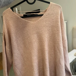 Ljusrosa stickad tröja Vero Moda - Mysig ljusrosa stickad tröja från Vero Moda med v-ringad hals och lång ärm. Tröjan har en ribbad struktur och är perfekt för lager-på-lager under kyliga dagar. Enkel och stilren design som passar till det mesta.