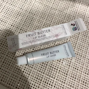 Fruit Butter Lip Mask från Seraphine - Fruit Butter Lip Mask från Seraphine Botanicals är en vegansk och cruelty-free läppmask i tub. Den är ljusgrå med svart text och kommer i en matchande kartong med blommönster. Perfekt för att återfukta och mjukgöra läpparna över natten.