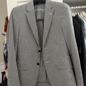 Randig kavaj från Bruun & Stengade - Snygg kavaj i slim fit från Bruun & Stengade, storlek 48. Kavajen har ett klassiskt randigt mönster i mörkblått och vitt, två knappar framtill och fickdetaljer med vit kant. Perfekt för dig som gillar stilrena och moderna plagg. Ny pris 1900