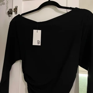 Svart offshoulder topp från 157 - Svart offshoulder topp från 157 med lång ärm och snygg rynkning i midjan. Modellen har en asymmetrisk halsringning som ger en cool vibe och sitter figurnära över kroppen. Perfekt att styla med vida byxor eller jeans för en trendig look.   Helt ny!! Säljer för att det inte var min typ av tröja men jätte snygg😍🥰 Ordinare pris- 150kr, säljer nu för 80 kr!! Pris går att diskutera 💕