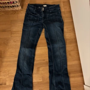 Blå bootcut jeans från Gina Tricot - Snygga blå jeans från Gina Tricot med bootcut passform och markerade sömmar. Modellen har stora fickor fram och bak, dubbla knappar i midjan och klassisk jeanslook. Lite defekter som man kan se på bilderna.